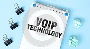 White notepad with text VOIP TECHNOLOGY and office tools on the blue background