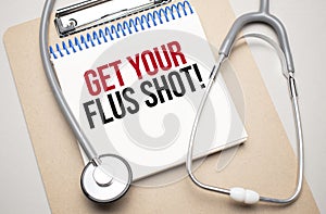 White notepad with the words get your flus shot and a stethoscope on a blue background. Medical concept