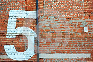 Painted white figure, number five on a red brick wall