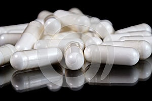 White oblong pharmaceutical capsules on reflective surface, black background