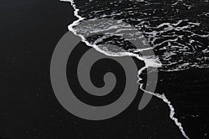 White ocean foam on black sand volcanic texture