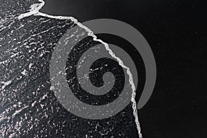 White ocean foam on black sand volcanic texture