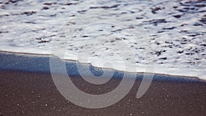 White ocean foam on black sand.