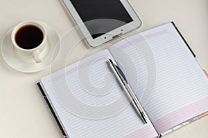 White office desk with necessary items on it. Diary with pen, Samsung phone. White cup of coffee. Top view with copy space