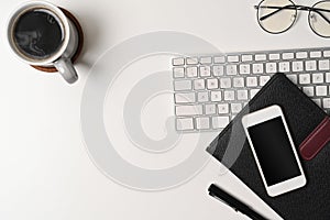 White office desk with smart phone, notebook, glasses and coffee cup.