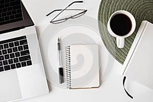 White office desk table with blank notebook, laptop computer, supplies and coffee cup, top view with copy space, modern workplace