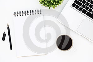 White office desk table with blank notebook page with pen, laptop and coffee. Top view with copy space, flat lay