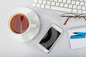 white office desk table with computer keyboard, smartphone, cup of tea