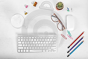 White office desk table with computer mouse and keyboard, cup of latte coffee, pencils and eye glasses. Top view with copy space,