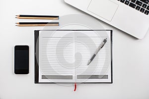 White office desk table with laptop, mobilephone, notebook, and