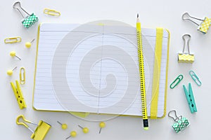 White office desk table with open notebook with empty pages and other office supplies. Top view