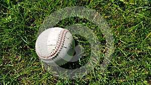 White old baseball ball on fresh green grass with copy space closeup. American sports baseball game