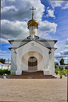 White old chapel with large wooden doors against the backdrop of green trees and blue sky