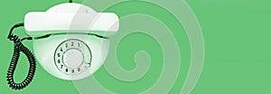 White old telephone with rotary dial on green background. Flat lay. Top view. Banner