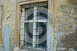 White old wooden window behind a brown rusty grate on the concrete wall