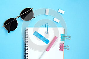 White open notebook with blue elements, gum and sunglasses on a light blue background