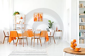 White and orange dining room with painting on the wall, bookshelf in the corner and green plant