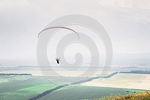 White orange paraglide with a paraglider in a cocoon against the background of fields of the sky and clouds. Paragliding