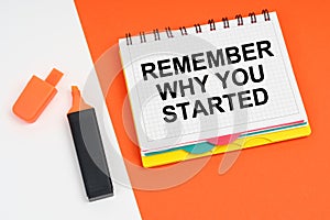 On a white-orange surface lies a marker and a notepad with the inscription - REMEMBER WHY YOU STARTED