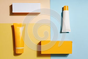 White and orange tubes and boxes of sunscreen on yellow and blue background. Sun Protection. Copy space. Top view