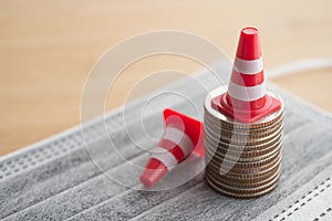 White orange under construction cone around stacked coins on mask. Global world economy crisis due to COVID-19, fix repair