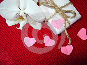 White orchid and gift box on a red background, Valentines Day background. Small paper hearts.