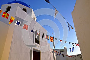 White orthodox church cathedral with blue dome and garland of flags of different countries on the blue sky.