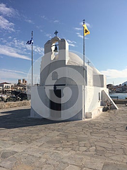 White othodox church, Greece, with a flags. White chapel on a shore.