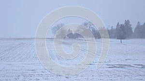 White-Out Snow Storm Blizzard Across Countryside and Farmhouse With Camera Pan.  Heavy Snowing Landscape of Rural Farm Field