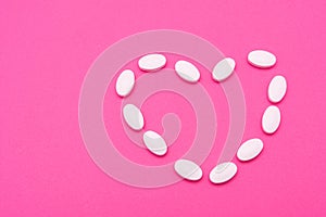 White oval pills lie on a pink background. Copy space, macro
