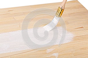 White paint with a brush painting a wooden background with texture