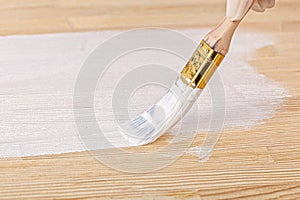 White paint with a brush painting a wooden background with texture