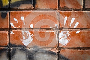 White paint prints of two hands on colourful graffity on a brick