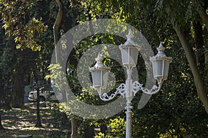 White painted old-style triple chandelier close-up. In the background are trees and a white car