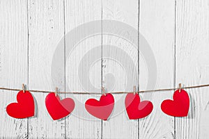 White painted wooden background with a garland of red hearts. Natural rope and clothespins. Concept of recognition of love,