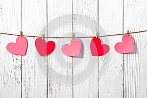 White painted wooden background with a garland of red and pink hearts. Natural rope and clothespins. Concept of recognition of