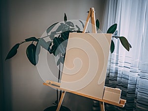 White painting board on a wooden easel near a green plant