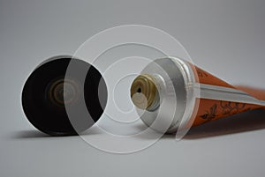 On a white paper background lies and is a tube from a female face cream with a dark brown lid, a cap