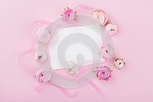 White paper blank and spring flower on pink desk from above for wedding mockup or greeting card on womans day. Floral frame.