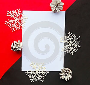 White paper blank and white snowflakes on geometric red and black abckground. Flat lay, top view, copy space.