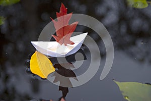 A white paper boat with an oak leaf instead of a sail on black water