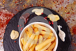 White paper bowl of french fries chipsWhite paper bowl of french fries chips potato and sauces on black stone slate over rusty