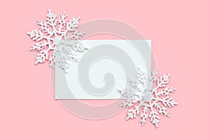 White paper card decorated with snowflakes on pink background. New Year, Christmas and winter concept. Flat lay, top view, free
