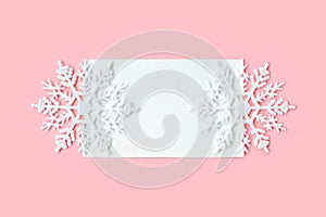 White paper card decorated with snowflakes on pink background. New Year, Christmas and winter concept. Flat lay, top view, free