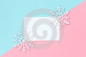White paper card decorated with snowflakes on pink and light blue background.