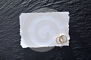 White paper card with two engagement rings on slate table