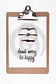 White paper on clipboard with real donut on it and wordplay text saying `Donut worry be happy`