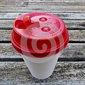White paper coffee cup with red travel lid on wooden table
