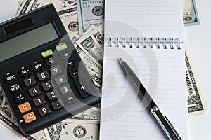 White paper note pad and pen, calculator on dollar banknotes using as business accounting or tax calculation concept