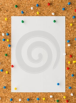 White paper note sheet with multicolored push pin on cork board